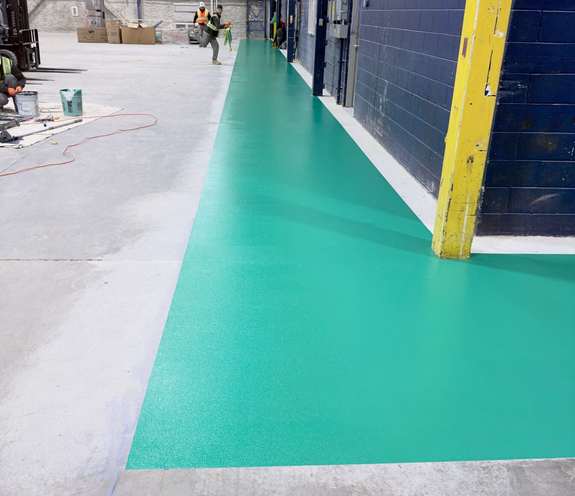 Green epoxy-coated industrial walkway with anti-slip finish installed on concrete floor inside warehouse, creating a clearly defined pedestrian path alongside workstations.