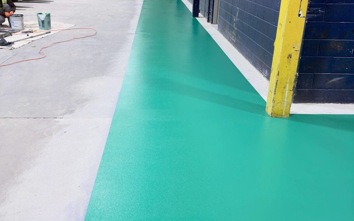 Green epoxy-coated industrial walkway with anti-slip finish installed on concrete floor inside warehouse, creating a clearly defined pedestrian path alongside workstations.